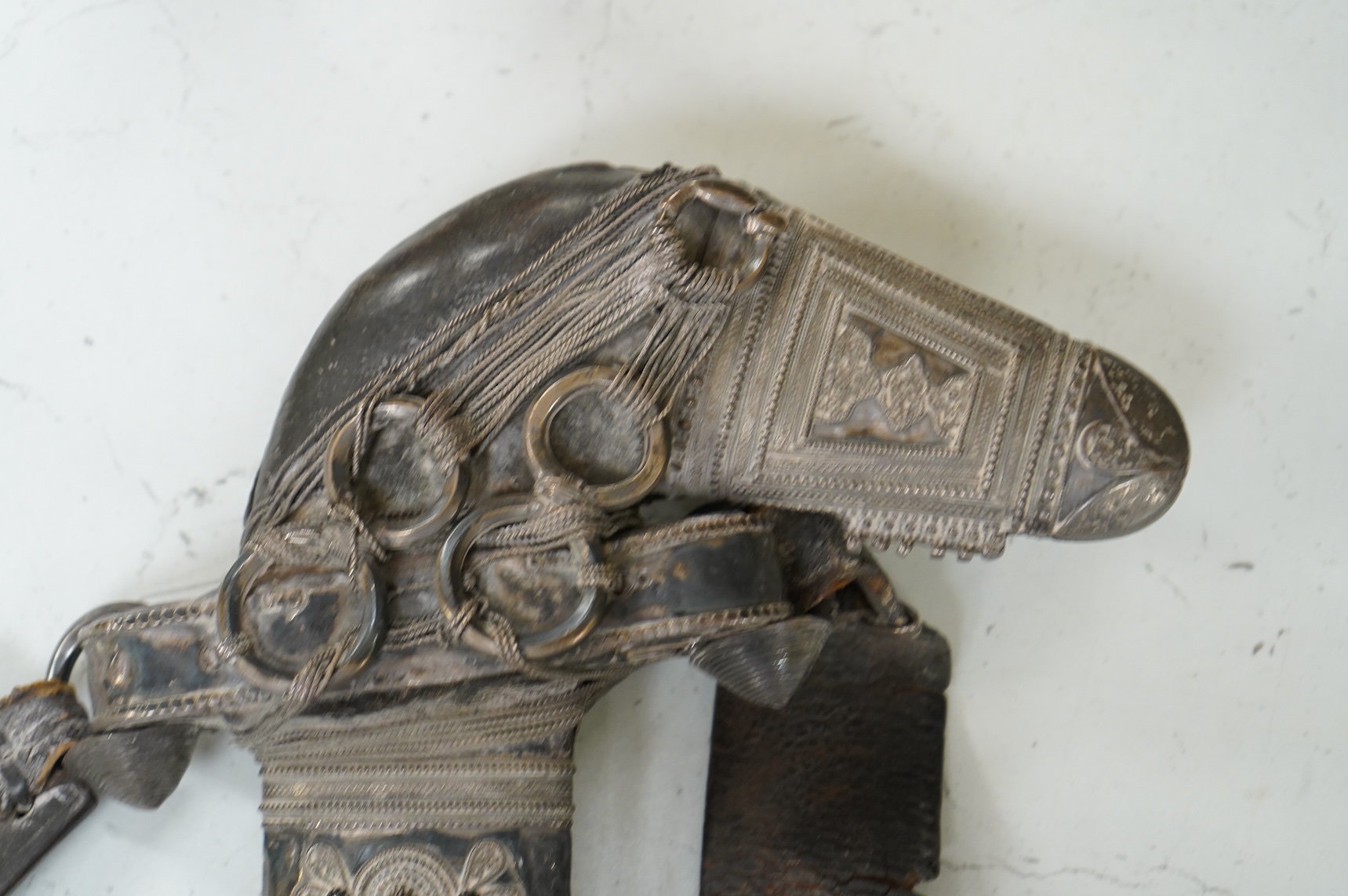 A late 19th century Arab silver mounted dagger jambya with silver filigree mounts to hilt and sheath, in its leather covered scabbard with parts of the original belt